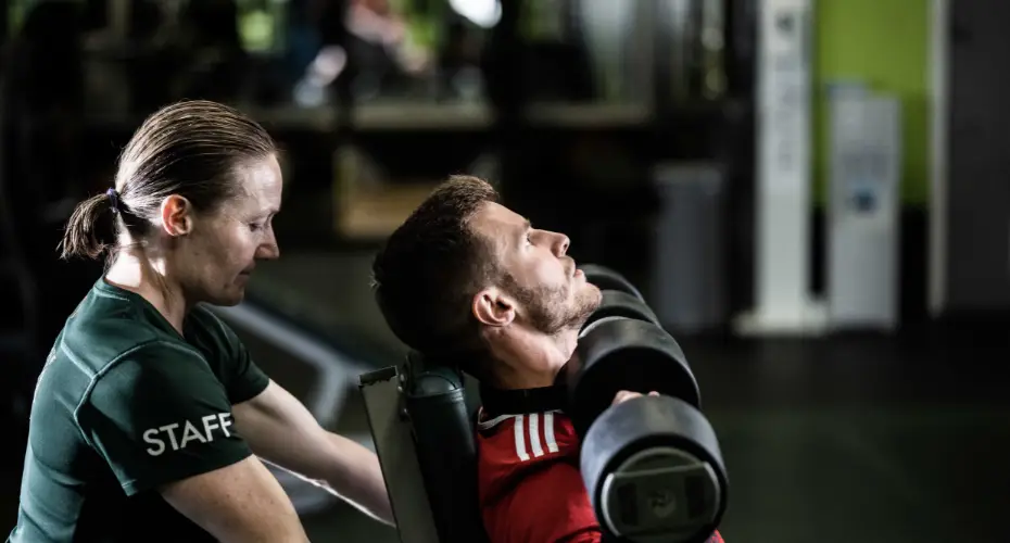 A staff member assisting a member of the gym with a workout.